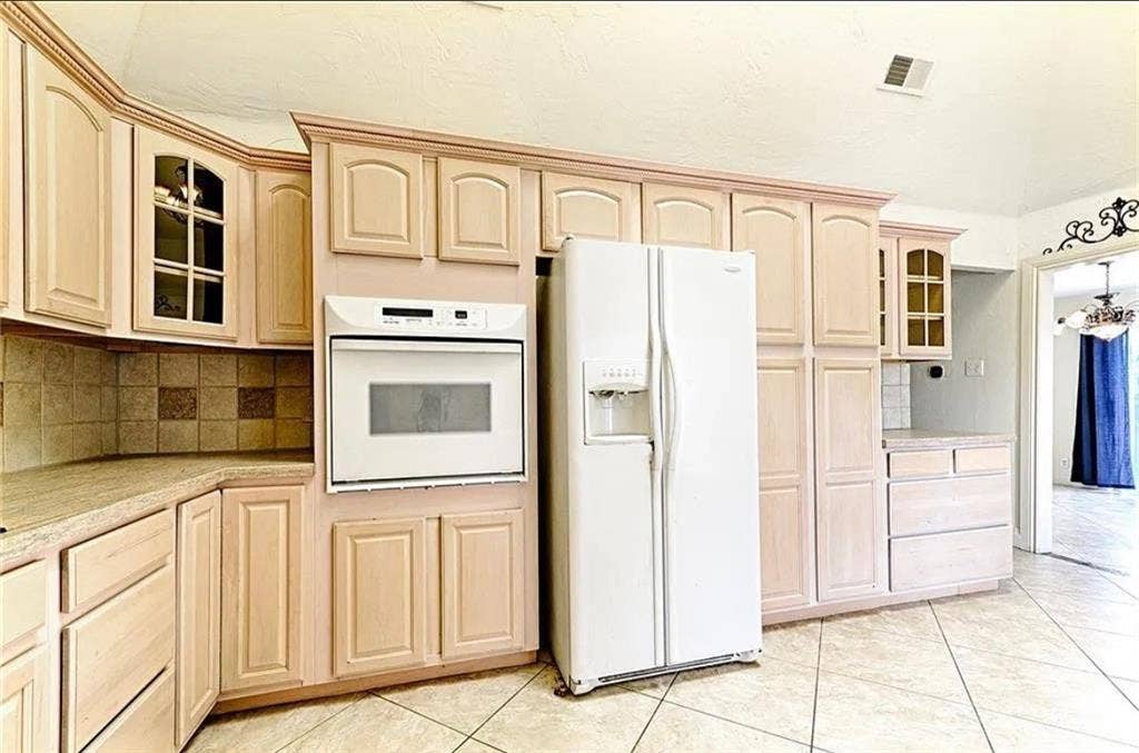 2601 Country Place, Carrollton, TX 75006 Spacious kitchen featuring light wood cabinetry with raised-panel doors, ceramic tile backsplash, white side-by-side refrigerator, white built-in wall oven with microwave, and neutral tile flooring throughout the cooking and dining area