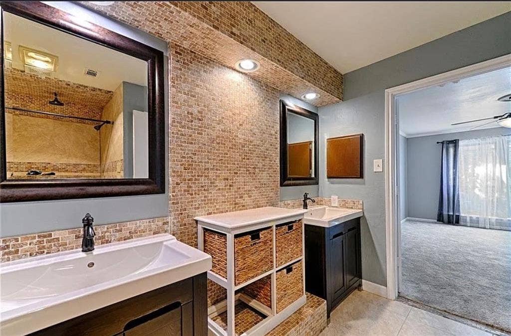 2601 Country Place, Carrollton, TX 75006 Master bathroom featuring dual vanities with wood-finish cabinetry and rectangular vessel sinks, brick accent wall with recessed lighting, large framed mirror, and tile flooring throughout