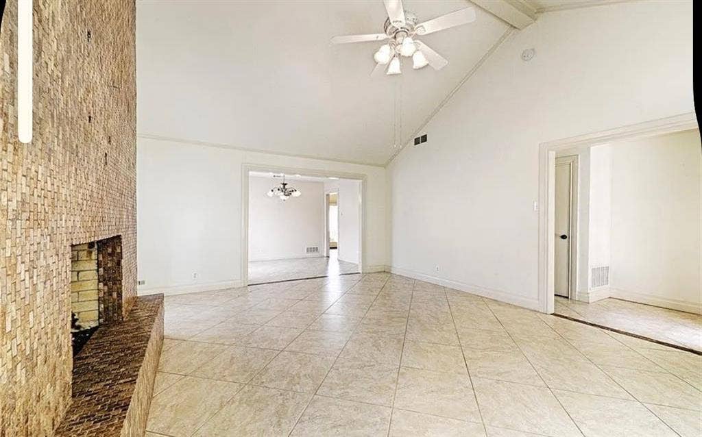 2601 Country Place, Carrollton, TX 75006 Spacious open-concept room featuring neutral tile flooring, vaulted ceiling with ceiling fan, exposed brick chimney with fireplace insert, and multiple entry points