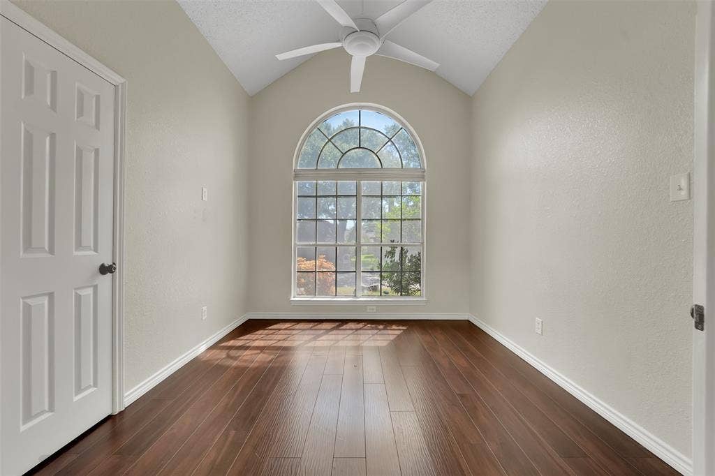 4001 Arrowcrest Lane, Garland, TX 75044 Bright, light-filled room featuring soaring vaulted ceilings with ceiling fan, rich wood-finish flooring throughout, and an exceptional arched transom window with multiple panes flooding the space with natural light