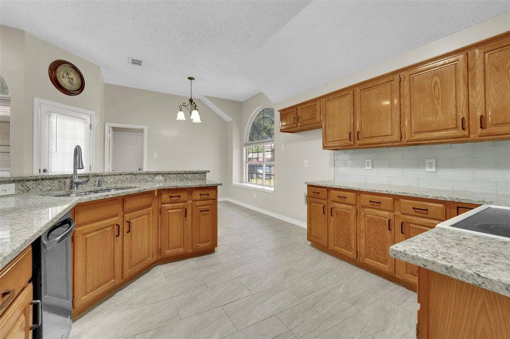 4001 Arrowcrest Lane, Garland, TX 75044 Spacious kitchen featuring warm wood cabinetry, granite countertops, stainless steel appliances, tile flooring, and abundant natural light from multiple windows