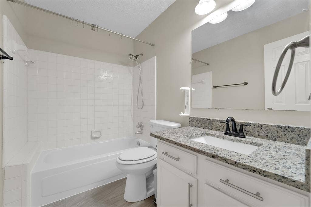 4001 Arrowcrest Lane, Garland, TX 75044 Modern bathroom featuring a white subway tile shower surround with frameless glass enclosure, dual-sink vanity with polished stone countertop, wood-finish flooring, and contemporary matte black hardware and fixtures throughout