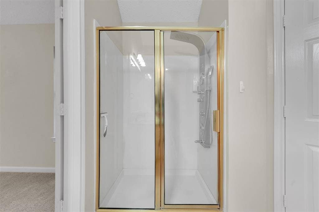 4001 Arrowcrest Lane, Garland, TX 75044 Frameless glass shower enclosure with brushed brass hardware and clean sightlines, positioned within a bright, neutral bathroom featuring white subway tile surround and soft natural lighting