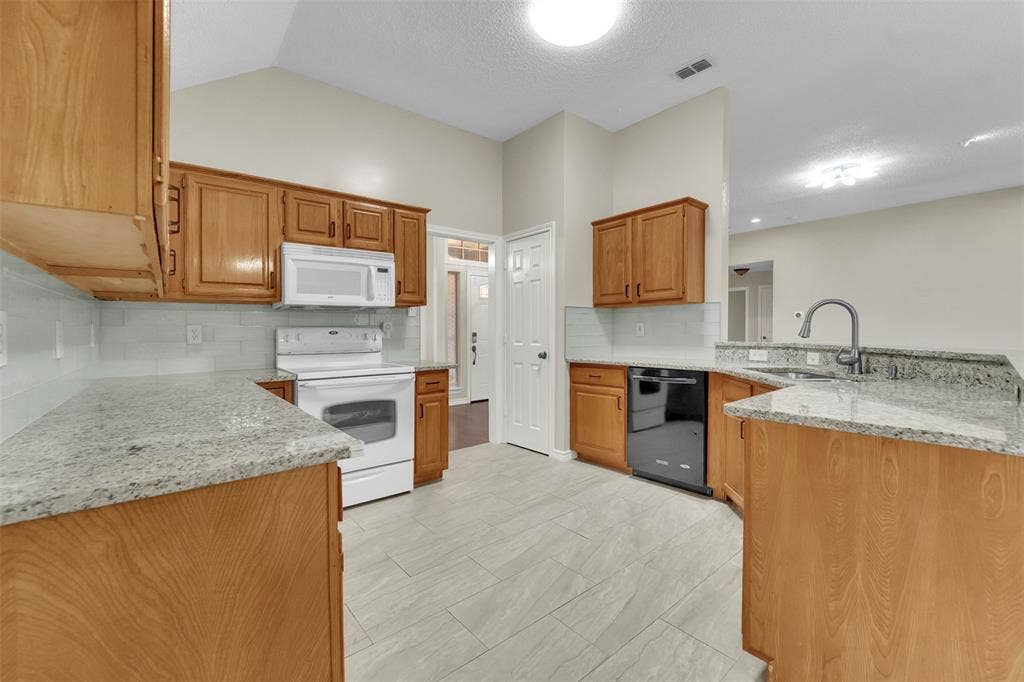 4001 Arrowcrest Lane, Garland, TX 75044 Spacious kitchen featuring warm wood cabinetry, granite countertops, stainless steel appliances, light wood-finish flooring, and recessed ceiling lighting throughout the open layout