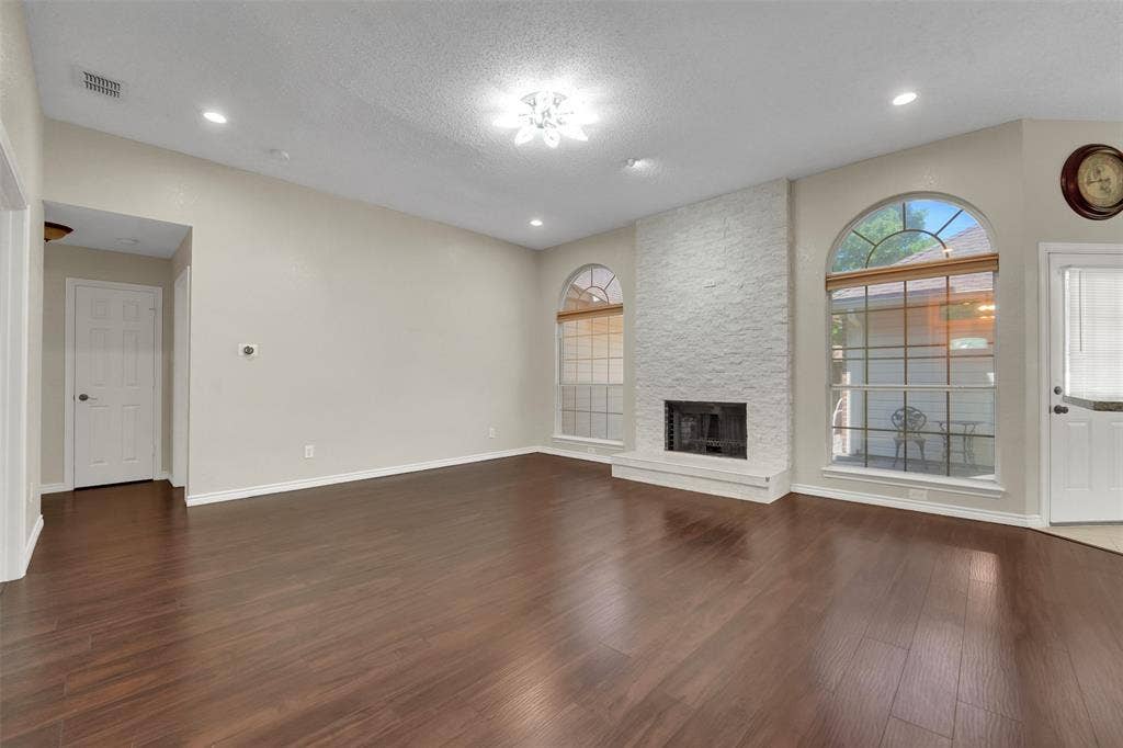 4001 Arrowcrest Lane, Garland, TX 75044 Spacious open-concept living area featuring rich wood-finish flooring, recessed ceiling lighting, and a striking brick fireplace with arched transom window