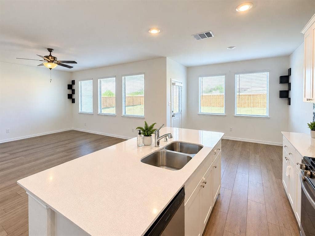 8432 Butterfly Lane, McKinney, TX 75071 Kitchen island with double basin stainless steel sink and light-toned countertop, wood-finish flooring, recessed lighting, ceiling fan, and multiple windows