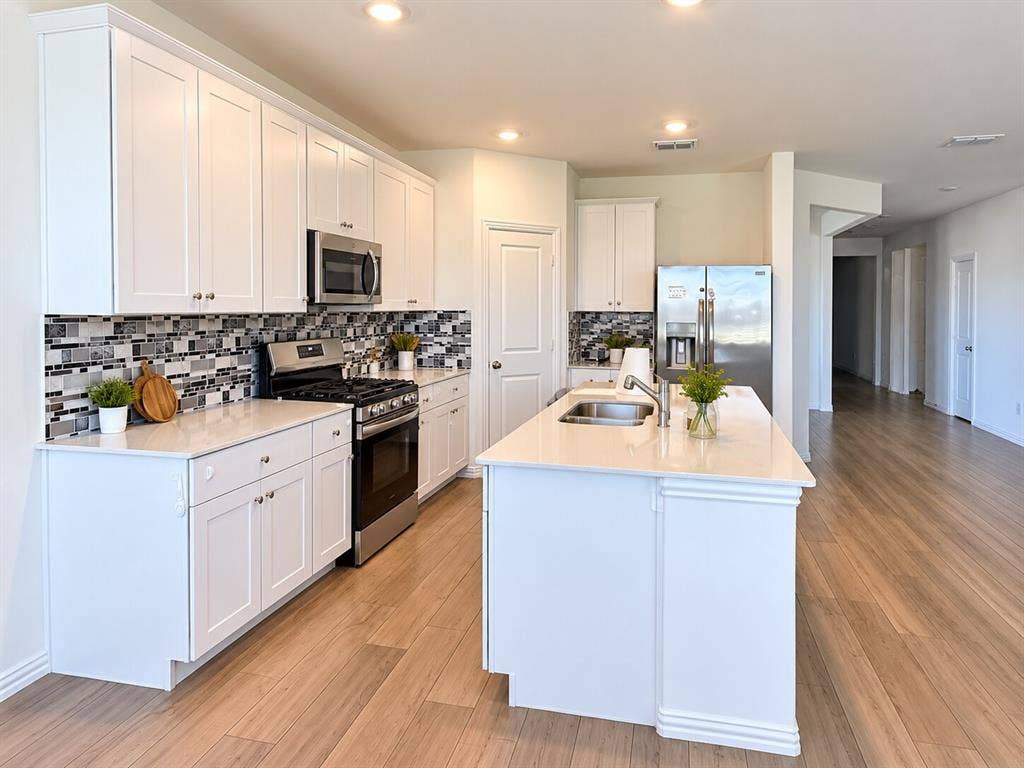 8432 Butterfly Lane, McKinney, TX 75071 White shaker cabinetry, stainless steel appliances, mosaic tile backsplash, central island with sink, and wood-finish flooring