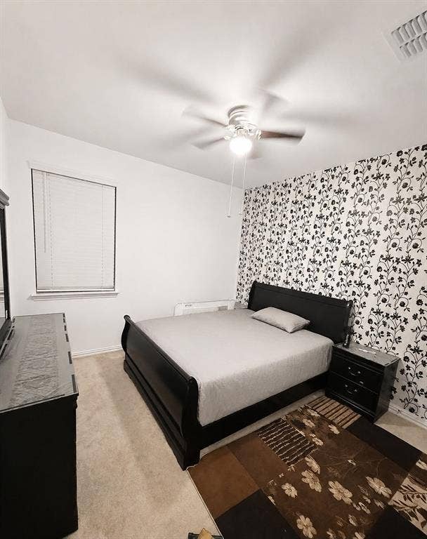 8432 Butterfly Lane, McKinney, TX 75071 Spacious bedroom featuring a black platform bed frame, wood-finish flooring, ceiling fan with integrated lighting, patterned accent wall, and a large window with natural light