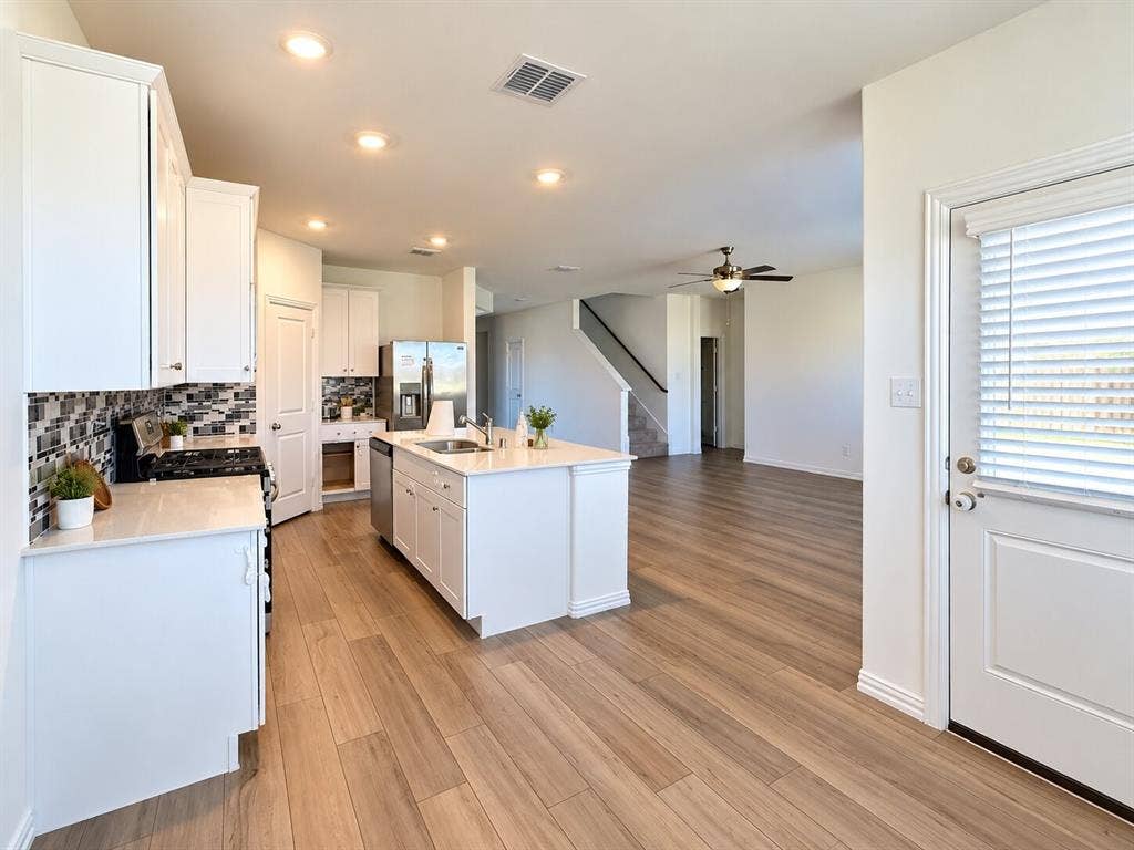 8432 Butterfly Lane, McKinney, TX 75071 Modern kitchen featuring white cabinetry, a central island with an integrated sink, mosaic tile backsplash, stainless steel appliances, and wood-finish flooring