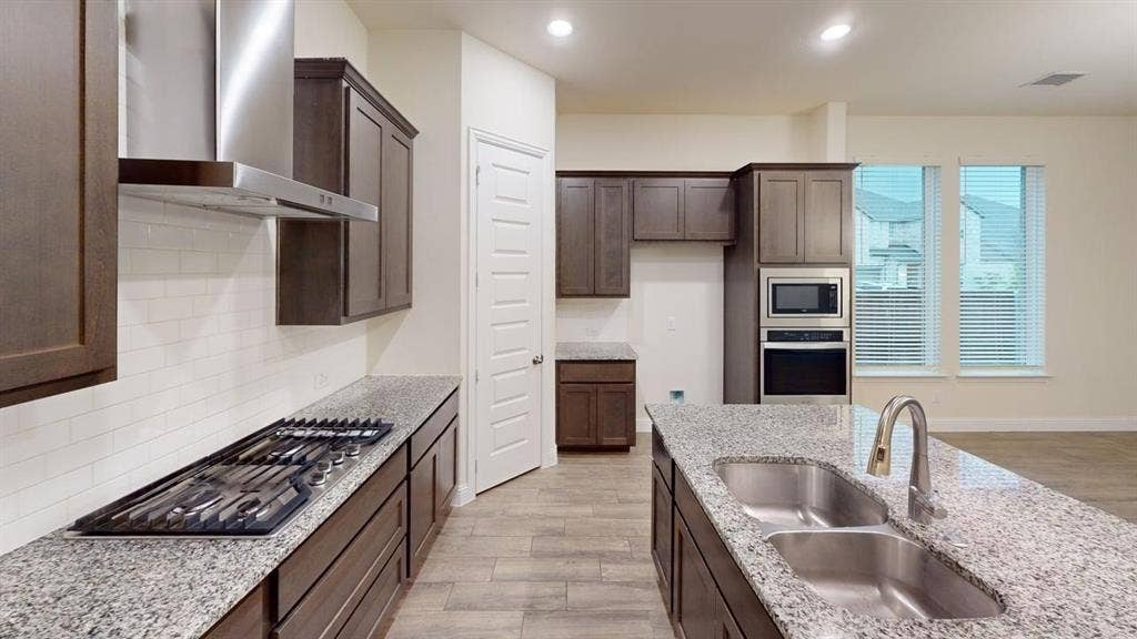 3314 Willena Road, Melissa, TX 75454 Kitchen featuring wood-finish cabinetry, granite countertops, tile backsplash, built-in stainless steel appliances, and a kitchen island with an undermount double sink