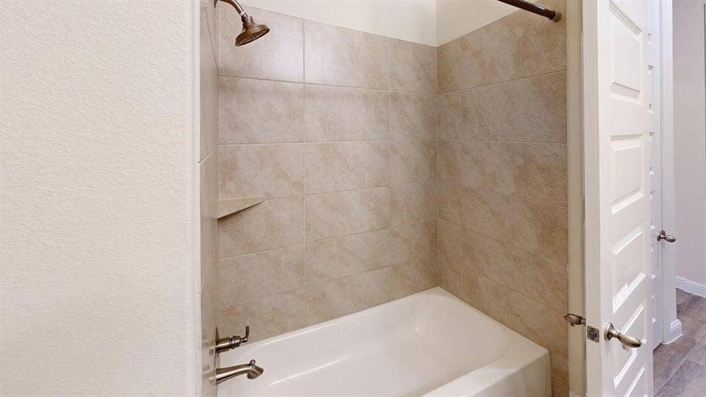 3314 Willena Road, Melissa, TX 75454 Updated primary bathroom featuring a tile-lined shower enclosure with brushed nickel fixtures, a white soaking tub with integrated surround, and neutral stone-finish wall treatments throughout