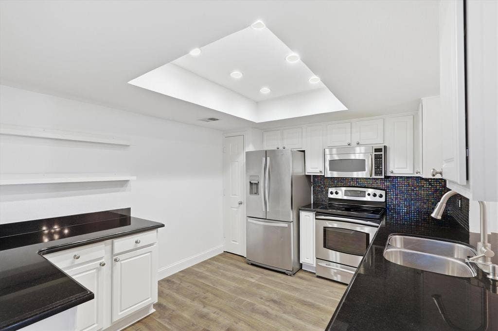 10207 Regal Oaks Drive, #109, Dallas, TX 75230 Bright kitchen with white cabinetry, dark countertops, stainless steel appliances and a exit door that brings natural light into the space.