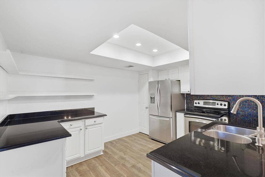 10207 Regal Oaks Drive, #109, Dallas, TX 75230 Kitchen view highlighting the white cabinetry, dark countertops, stainless steel appliances and abundant light.