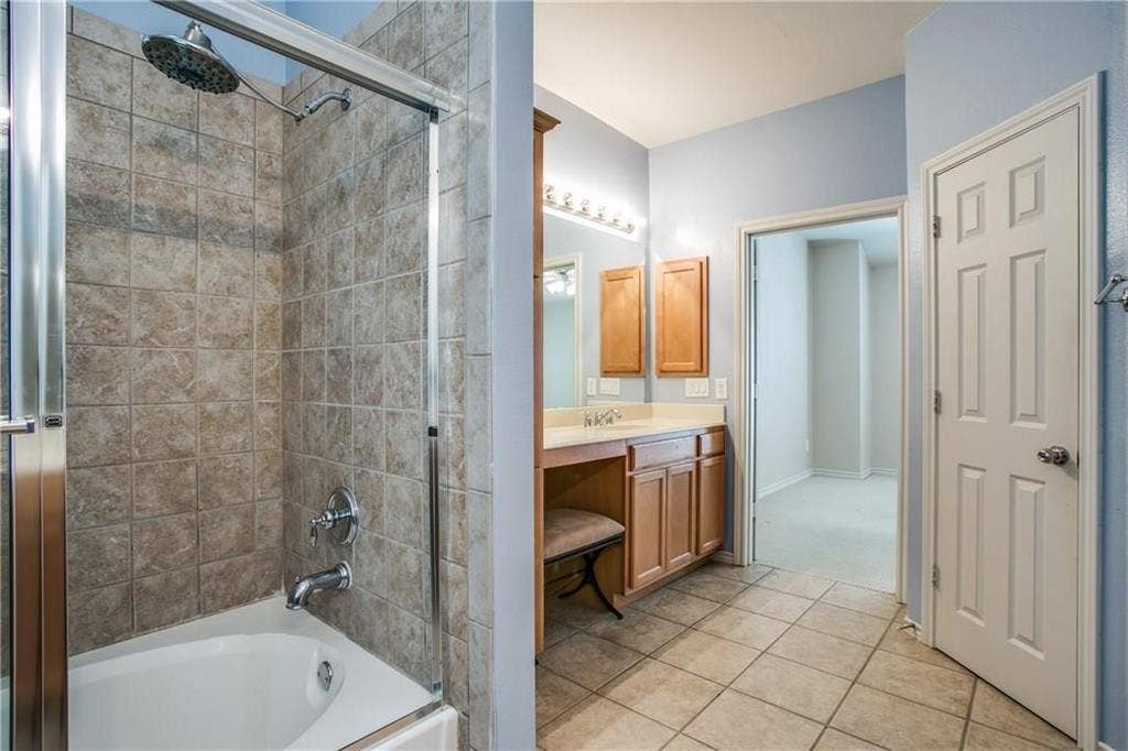 2415 Stutz Drive, #D, Dallas, TX 75235 Tub and shower combination with tiled surround, glass enclosure, wood-finish vanity with countertop, and tile flooring