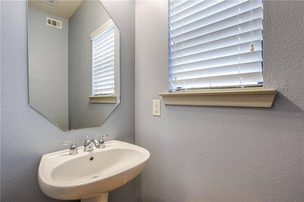 2415 Stutz Drive, #D, Dallas, TX 75235 Pedestal sink with chrome fixtures, an octagonal mirror, and a window with blinds