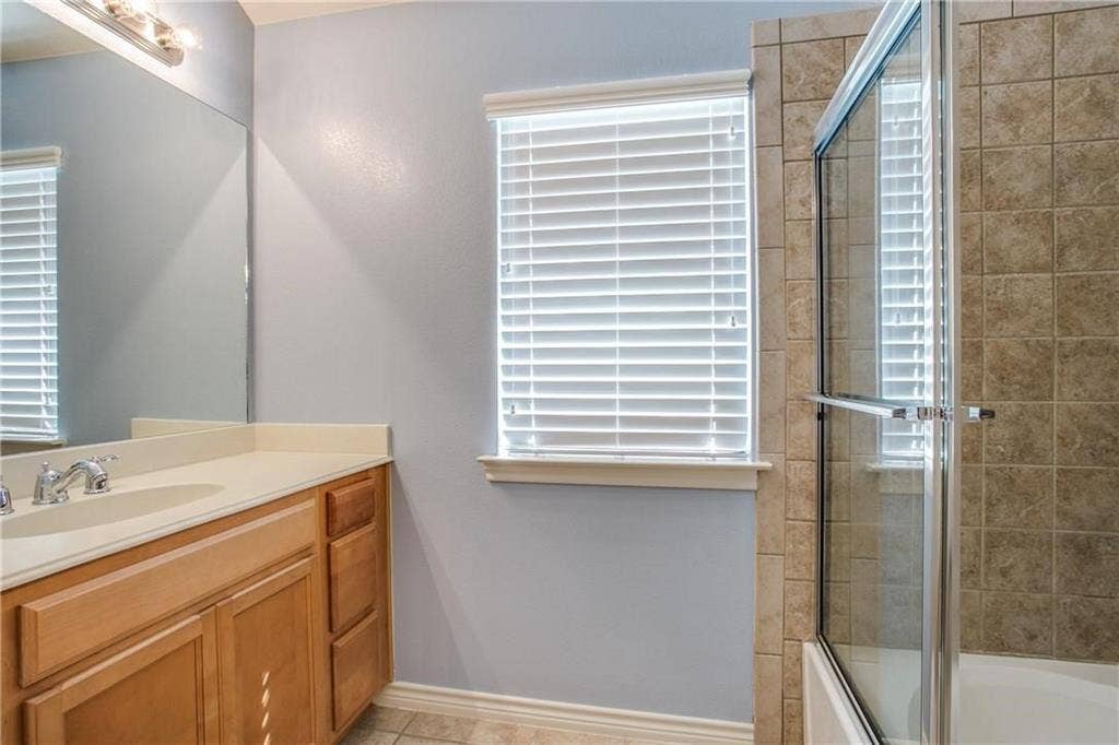 2415 Stutz Drive, #D, Dallas, TX 75235 Bathroom featuring a vanity with an integrated sink, wood-finish cabinetry, and a tile-surround shower with a glass enclosure