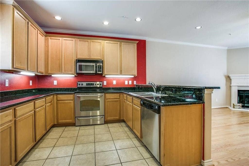 2415 Stutz Drive, #D, Dallas, TX 75235 U-shaped kitchen featuring wood-finish cabinetry, dark countertops, stainless steel appliances, and tile flooring