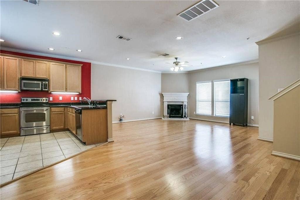 2415 Stutz Drive, #D, Dallas, TX 75235 Open-concept living area with wood-finish flooring, a kitchen featuring stainless steel appliances, and a fireplace with a detailed mantel