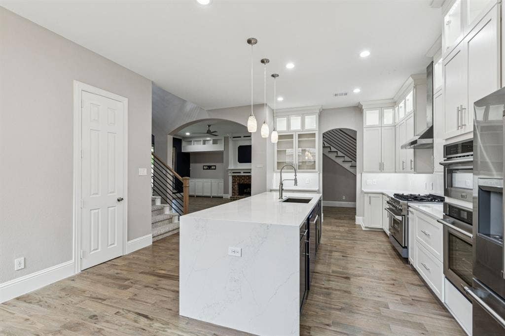 15456 Mountain View Lane, Frisco, TX 75035 Gourmet kitchen featuring a large central island with sink, stainless steel appliances, white cabinetry with glass-front uppers, and wood-finish flooring