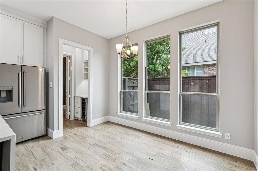 15456 Mountain View Lane, Frisco, TX 75035 Wood-finish flooring, three large windows, stainless steel refrigerator, white cabinetry, and a contemporary chandelier