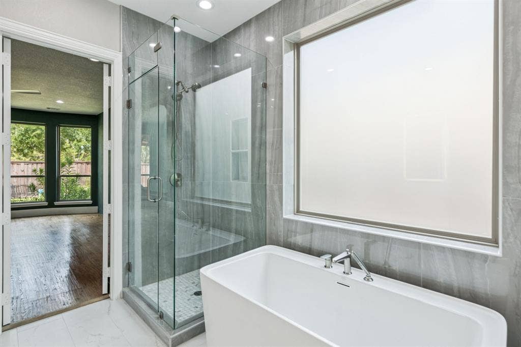 15456 Mountain View Lane, Frisco, TX 75035 Spa-inspired primary bathroom featuring a freestanding soaking tub, frameless glass shower enclosure with tile surround, dual vanity with integrated sink, polished chrome fixtures, recessed ceiling lighting, and access to an outdoor garden space through French doors