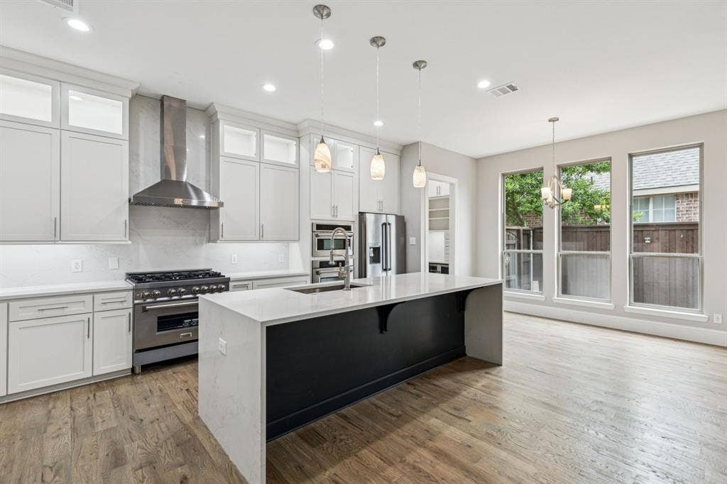 15456 Mountain View Lane, Frisco, TX 75035 Gourmet kitchen featuring white shaker cabinetry, stainless steel appliances, a center island with a waterfall countertop, and wood-finish flooring