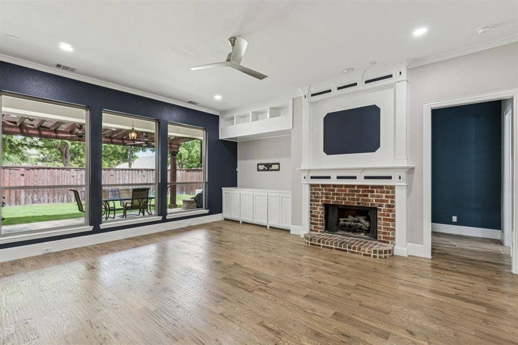 15456 Mountain View Lane, Frisco, TX 75035 Wood-finish flooring, a brick fireplace with a white mantel, expansive windows, built-in cabinetry, and recessed lighting