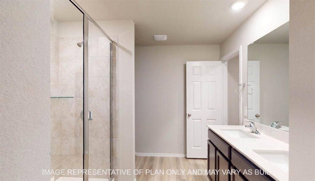 3112 Cyprian Road, Lorena, TX 76655 Spa-inspired primary bathroom featuring a frameless glass shower enclosure with tile surround, dual-sink vanity with wood-finish cabinetry and white quartz countertop, large mirror with integrated lighting, and neutral tile flooring throughout