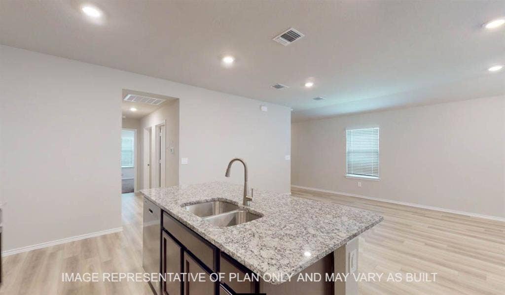 3112 Cyprian Road, Lorena, TX 76655 Modern kitchen and open living area featuring a dual-basin stainless steel sink, polished stone countertops, contemporary faucet with pull-down spray, light wood-finish flooring, recessed ceiling lighting, and abundant natural light from multiple windows