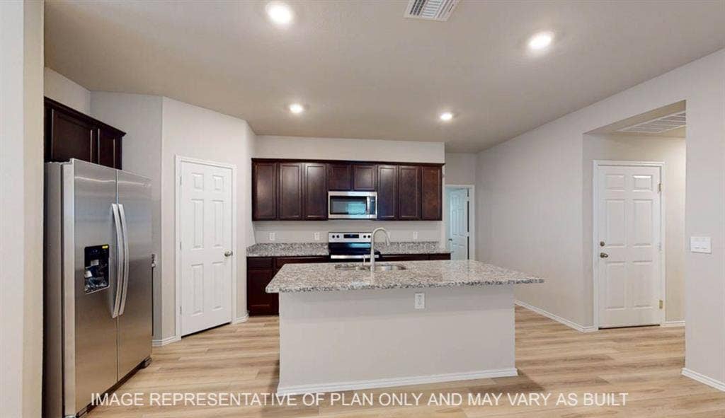 3112 Cyprian Road, Lorena, TX 76655 Modern kitchen featuring dark cabinetry, stainless steel appliances including a side-by-side refrigerator and microwave, granite-look countertops, and a white island with breakfast bar seating