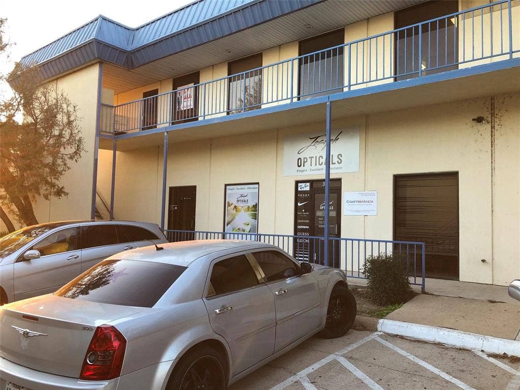 1039 N Interstate 35 Highway N, #E, Carrollton, TX 75006 Two-story commercial building featuring light-colored exterior walls, a blue metal roof, and a second-story balcony with metal railings