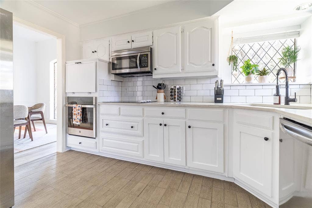 3612 Tumbril Lane, Plano, TX 75023 White cabinetry with black hardware, subway tile backsplash, stainless steel microwave, built-in oven, and wood-finish flooring