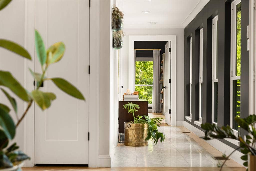 9863 Elmcrest Drive, Dallas, TX 75238 Large hallway off the foyer features an accented wall with multiple vertical windows. A guest bathroom and hidden stairs to private study are along the left side with end of hallway leading to the primary suite.
