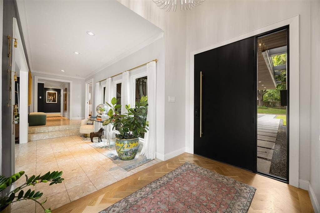 9863 Elmcrest Drive, Dallas, TX 75238 Foyer featuring a modern entry door with a vertical brass pull handle, a full-height sidelight, and herringbone wood flooring. Two steps lead to guest suite on the right overlooking front courtyard.
