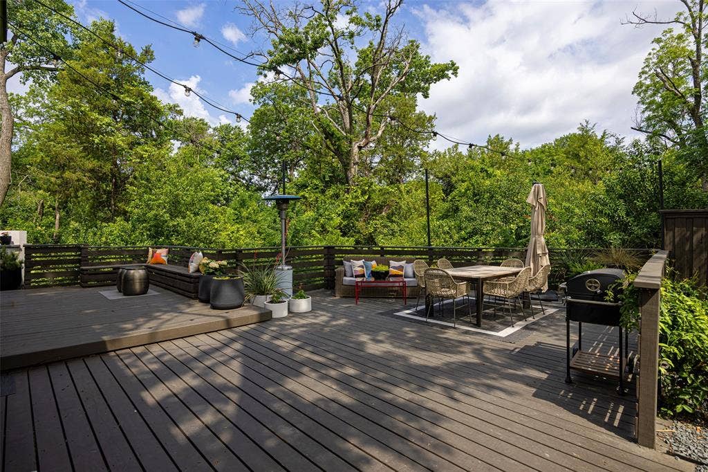 9863 Elmcrest Drive, Dallas, TX 75238 Enhance your outdoor dining experience with the large deck featuring wide planks and perimeter fence set against a backdrop of trees and creek.