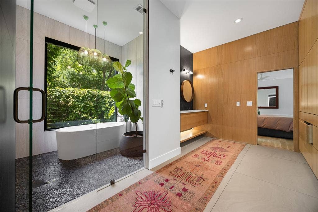 9863 Elmcrest Drive, Dallas, TX 75238 Spa like primary bathroom featuring a wet room with freestanding soaking tub, floor-to-ceiling glass-enclosed shower with pebble flooring, and a large window offering exterior views.