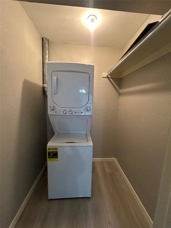 5826 Sandhurst Lane, #C, Dallas, TX 75206 Dedicated laundry area featuring a stacked washer and dryer, wood-finish flooring, and overhead shelving