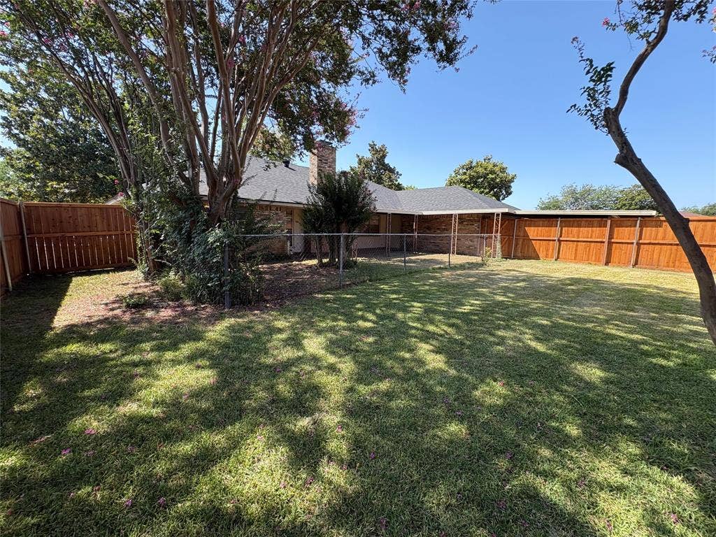 1025 Cloverdale Lane, DeSoto, TX 75115 Expansive backyard featuring a manicured lawn, wood fencing, covered patio, and mature trees