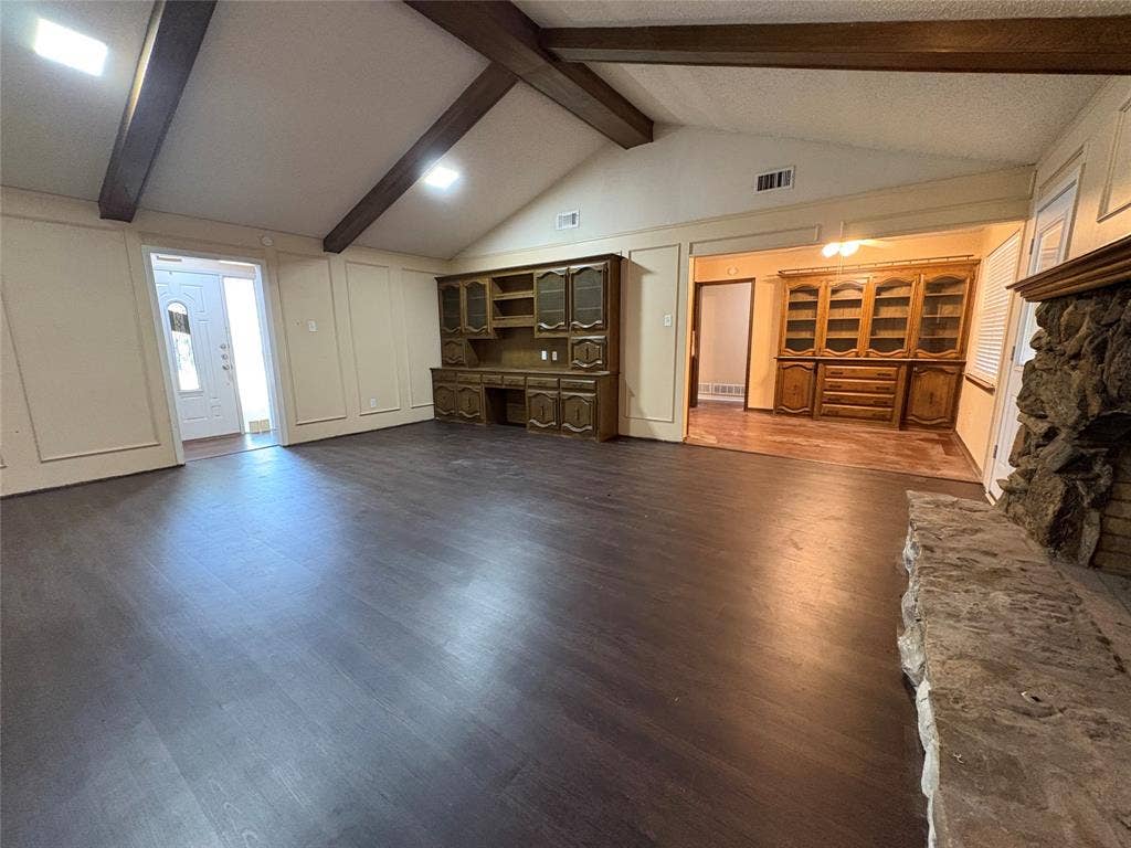 1025 Cloverdale Lane, DeSoto, TX 75115 Vaulted ceiling with exposed wood beams, wood-finish flooring, built-in custom cabinetry, and a stone-faced fireplace with a stone hearth