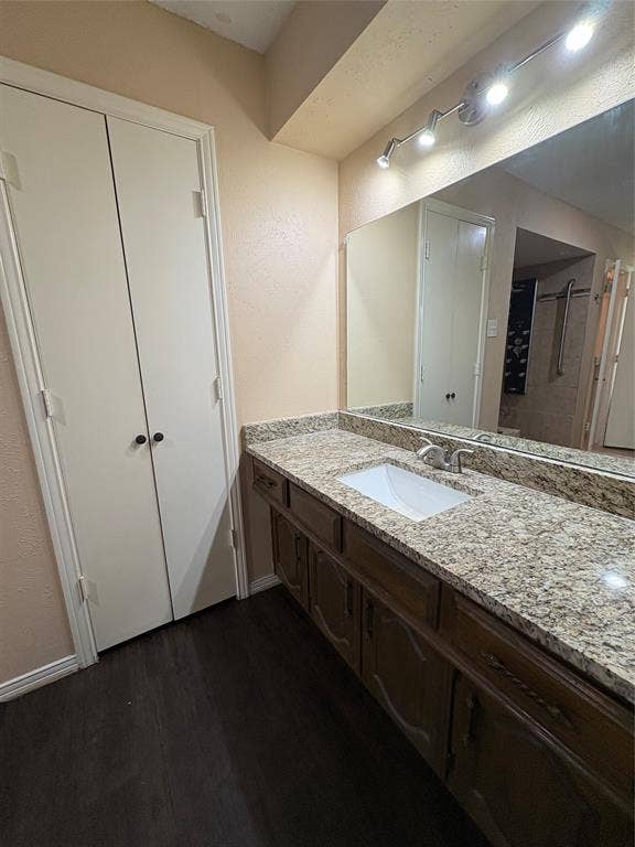 1025 Cloverdale Lane, DeSoto, TX 75115 Wood-finish flooring, vanity with granite-style countertop, integrated rectangular sink, track lighting, and full-width mirror