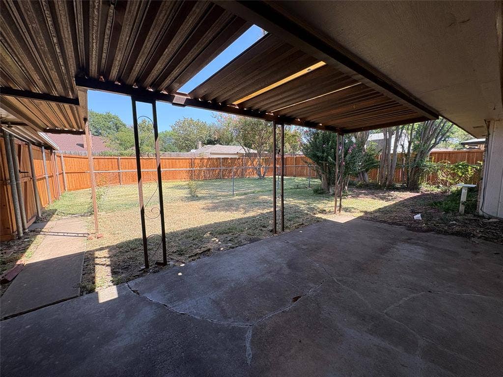 1025 Cloverdale Lane, DeSoto, TX 75115 Covered patio with concrete flooring, framed by a wood fence, leading to a grass area