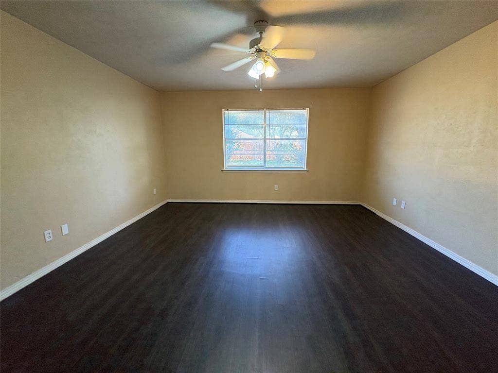 1025 Cloverdale Lane, DeSoto, TX 75115 Spacious room featuring dark wood-finish flooring, a ceiling fan with integrated lighting, and a window with white trim