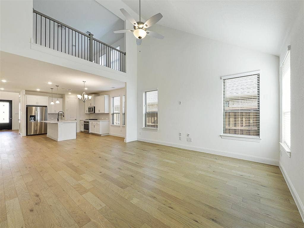 8305 Pine Island Way, McKinney, TX 75071 Vaulted ceiling with a ceiling fan, light wood-finish flooring, white kitchen cabinetry, kitchen island with a sink, and stainless steel appliances