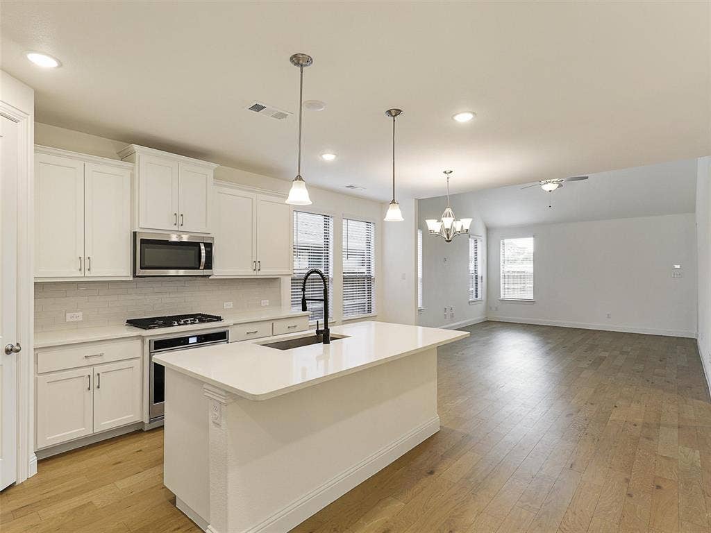 8305 Pine Island Way, McKinney, TX 75071 Kitchen island with pendant lighting, white cabinetry, integrated stainless steel appliances, and wood-finish flooring throughout