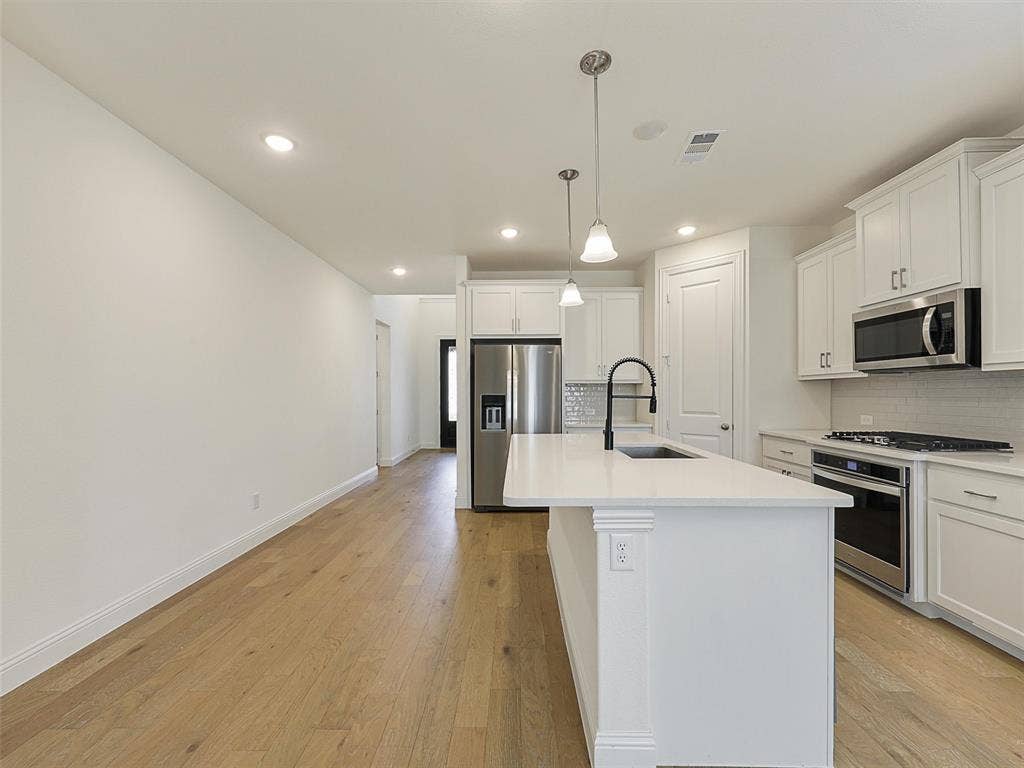 8305 Pine Island Way, McKinney, TX 75071 Kitchen featuring white cabinetry, quartz countertops, stainless steel appliances, and a central island with an undermount sink and matte black faucet