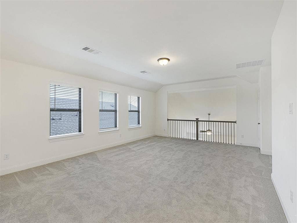8305 Pine Island Way, McKinney, TX 75071 Spacious carpeted room featuring three windows with blinds and a railing overlooking a lower level