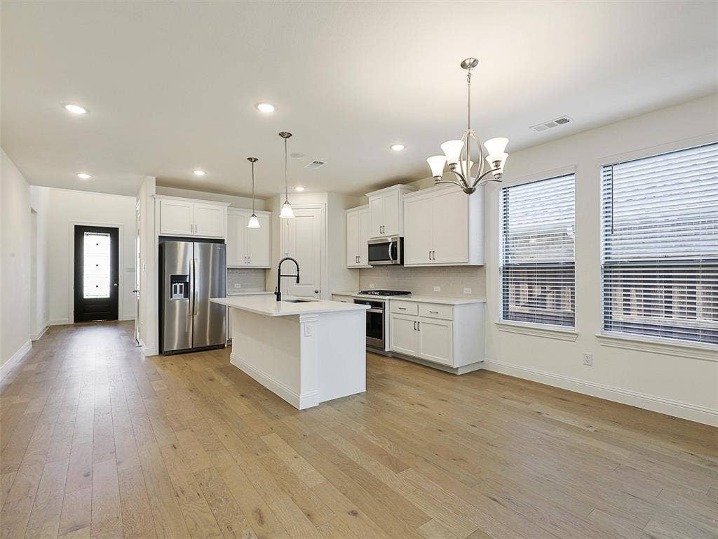 8305 Pine Island Way, McKinney, TX 75071 Open-concept living area featuring wood-finish flooring, a kitchen island with pendant lighting, white cabinetry, stainless steel appliances, and a dining area with a chandelier