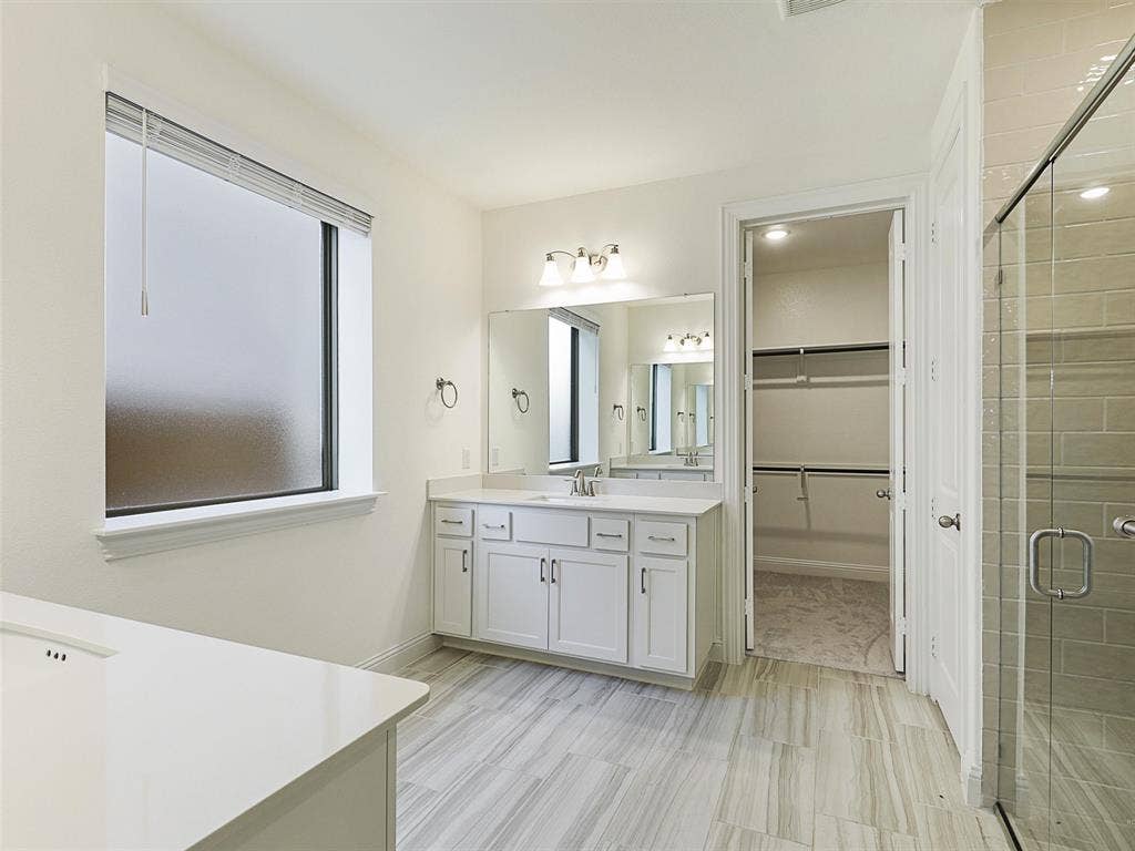 8305 Pine Island Way, McKinney, TX 75071 Spacious bathroom featuring a double vanity with ample storage, a glass-enclosed shower, wood-finish tile flooring, and a walk-in closet with built-in shelving