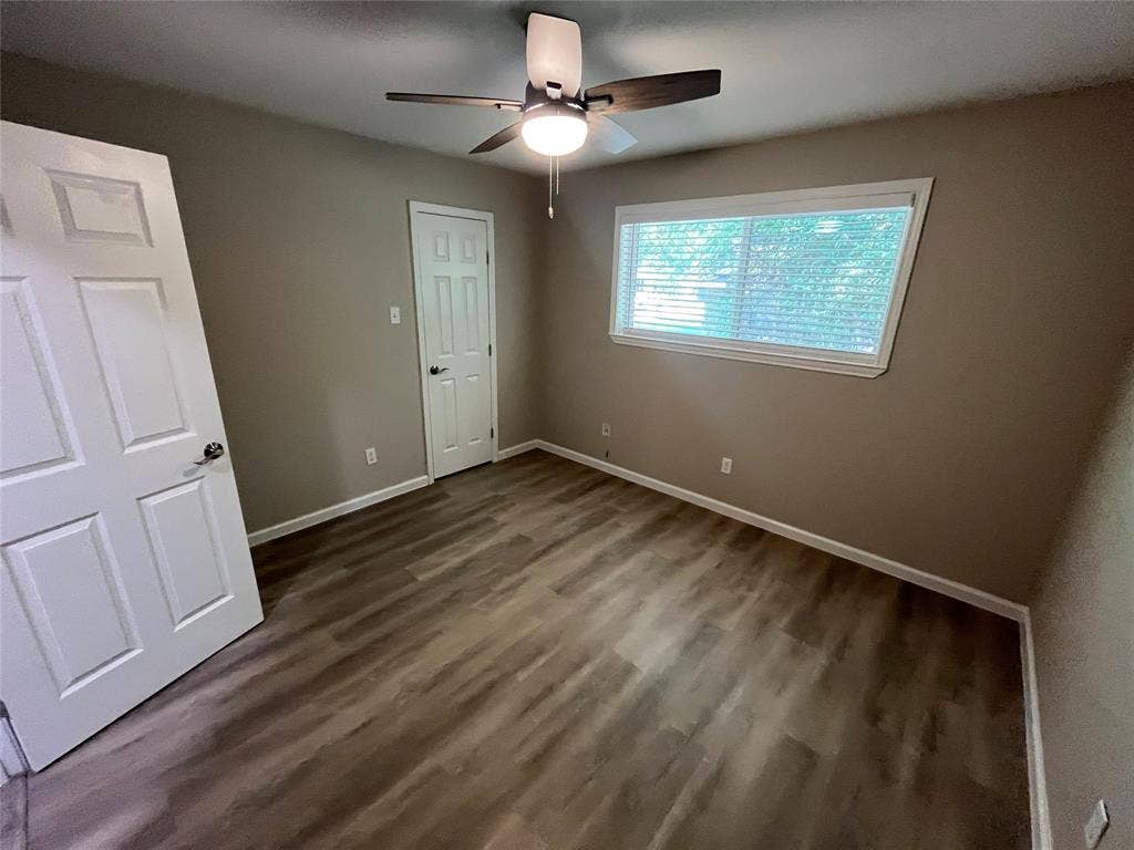 Room featuring wood-finish flooring, a ceiling fan with integrated lighting, and a window with horizontal blinds