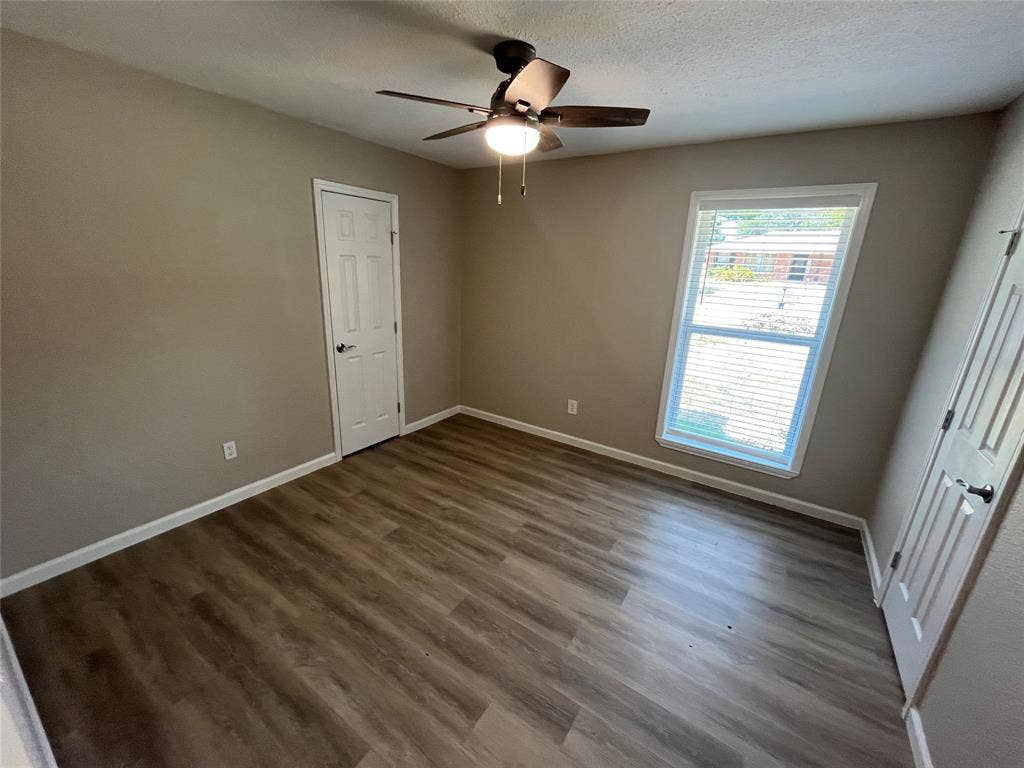 Wood-finish flooring, neutral wall tones, ceiling fan with integrated lighting, and window with blinds